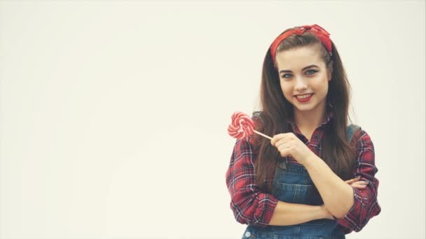 Krásná svůdná dívka stojící s červeným lízátkem ve tvaru srdce, usmívající se a pózující. — Stock video