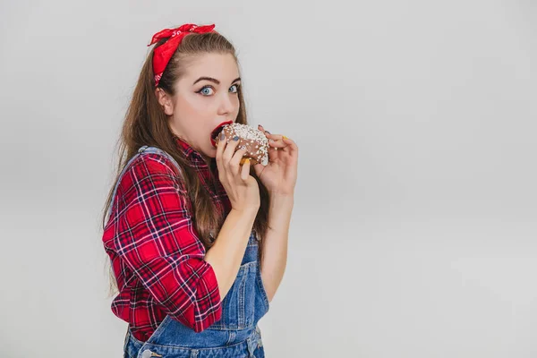 好奇心旺盛な若い女性が大きなチョコレートドーナツを食べ、まるで誰かから隠れているかのようにこっそり. — ストック写真