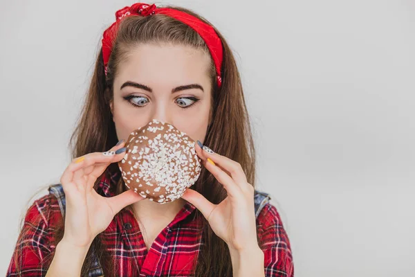 Belle jeune femme tenant un gros beignet au chocolat devant sa bouche, le sentant, appréciant son arôme incomparable . — Photo