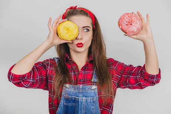 Kindisches junges Mädchen versteckt ihr Auge hinter großen Donut mit gelbem Zuckerguss, hält rosa Donut in der Nähe des Kopfes, macht Entengesicht. — Stockfoto