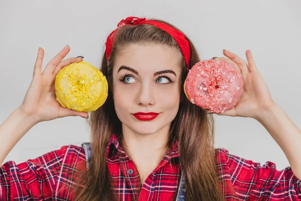 Lustige schöne Mädchen spielt herum und hält zwei süße Donuts in der Nähe der Ohren, die wie Tscheburaschka aussehen. — Stockfoto