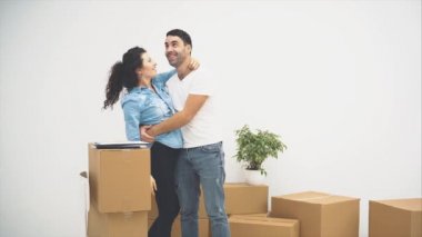 Genç çift yeni bir daireye taşınıyor. Kucaklaşan ve sarılan bir çift. Kutulardaki bazı kağıtları fark ettiler ve onları incelediler. 4k.