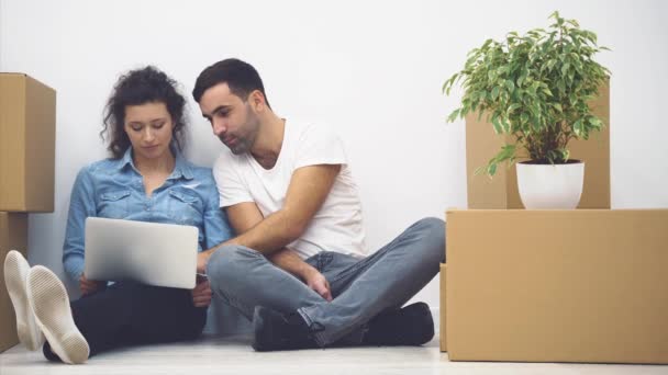 Pareja joven se muda a un nuevo apartamento juntos. Ellos están pensando de qué empezar, mirando a la pantalla del ordenador portátil. 4K . — Vídeos de Stock