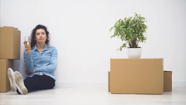Az ifjú hölgy a padlón ül. Van egy csomó meztelen doboz és egy növény a közelében. Másold a helyet. 4k. — Stock videók