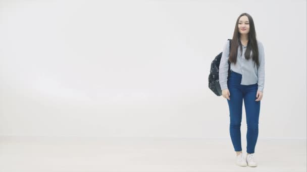 Bella sorridente asiatica giovane adolescente studentessa del liceo indossa jeans e camicia di jeans blu, zaino della scuola sopra la spalla. Guardando di lato, annuendo con la testa, alzando il pollice . — Video Stock