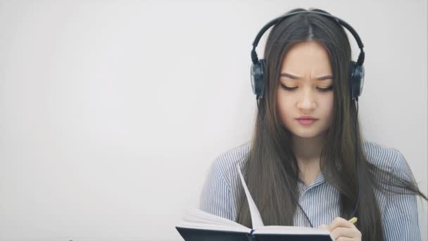 Inspirierte junge Asiatin, die mit Kopfhörern auf dem Boden sitzt, Musik hört, schreibt, Lieder umschaltet, tanzt. — Stockvideo