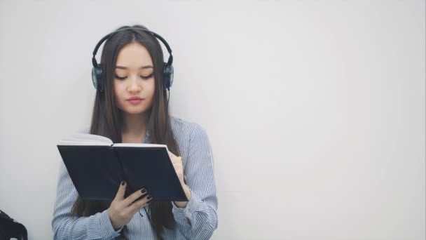 Inspirado jovem asiático menina sentado no chão em fones de ouvido, ouvir a música, pára de escrever e leva selfie . — Vídeo de Stock