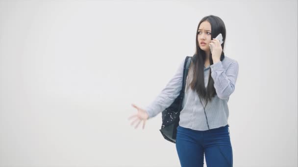 Érzelmes, fiatal ázsiai lány van a vonalban, problémákról beszél, integet a kezével, zaklatottnak tűnik. Hátizsák a válla fölött.. — Stock videók