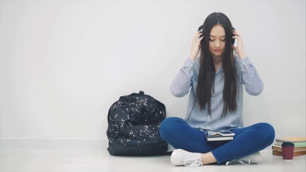 Zainspirowana młoda azjatycka dziewczyna w słuchawkach, słuchając muzyki, siedząc w pozycji lotosu. — Wideo stockowe