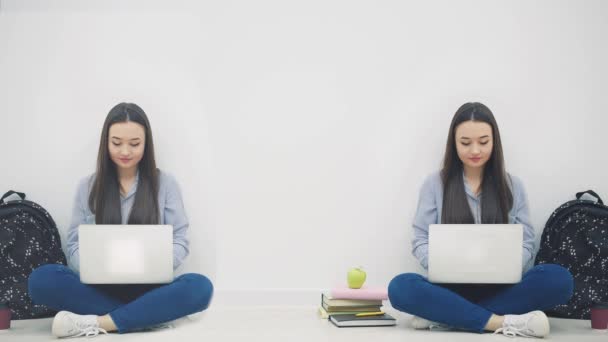 Twee mooie Aziatische meisjes zitten op de vloer in lotos positie met laptops, knikken met hun hoofd, zwaaien hallo, glimlachen. — Stockvideo