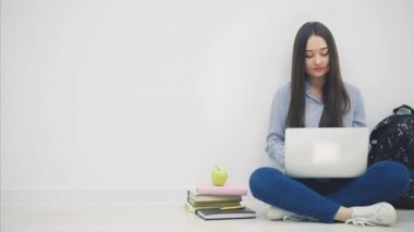 Güzel genç Asyalı bayan loto pozisyonunda dizüstü bilgisayarla yerde oturuyor, parmaklarını kameraya doğrultuyor, sonra da gülümsüyor..
