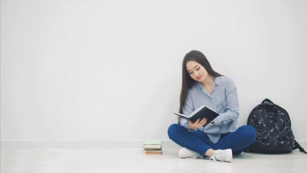 Jeune fille asiatique impliqué dans le processus de lecture livre, fermant itand étreignant, tout en étant assis sur le sol en position lotos . — Video