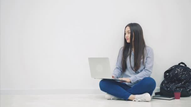 Mooie jonge aziatische dame zit op de vloer in lotos positie, met laptop, kijken naar de zijkant, geven duim omhoog, glimlachen. — Stockvideo