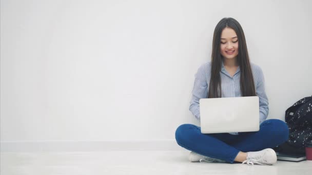 Härlig ung asiatisk dam sitter på golvet i lotos position, söker på internet, täcker sin mun med en hand förvånad med något. — Stockvideo