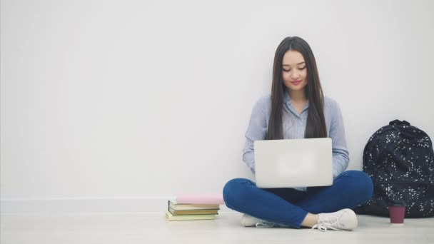 Jonge Aziatische dame zit op de vloer in loto positie, zoekt iets in haar laptop, haalt appel uit haar tas, zet het op de stapel boeken. — Stockvideo