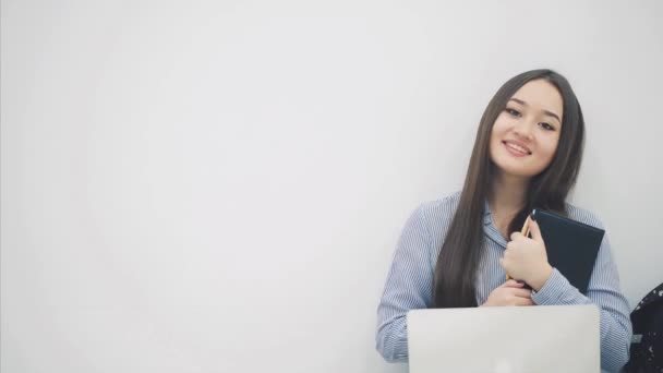 Güzel genç Asyalı bayan dizüstü bilgisayarla yerde oturuyor, elinde not defteri, parmağını yan tarafa gösteriyor.. — Stok video