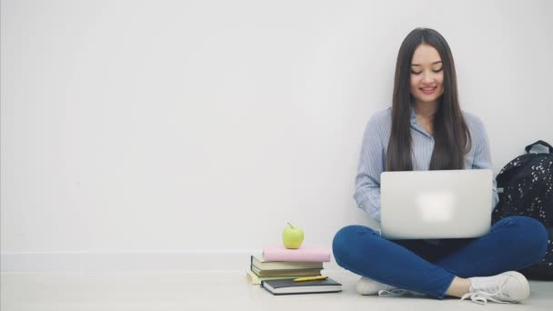 Mooie jonge Aziatische dame zit op de vloer in lotos positie, met laptop, wijzend haar vingers naar de camera, dan naar de zijkant, glimlachend. — Stockvideo