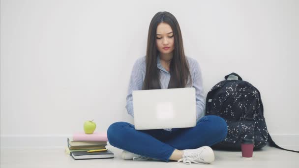 Young asian lady sitting on the floor in lotos position, with laptop, doesnt understand something, shrugging her shoulders, throwing hands. — Stock Video