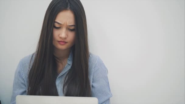 Härlig men trött asiatisk flicka sitter med laptop på knäna, har vissa svårigheter, skakar på huvudet, justera håret, ser upprörd. — Stockvideo