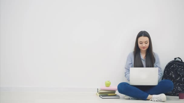 Belle jeune femme asiatique assise sur le sol en position lotos, cherchant sur Internet, saluant. Fournitures scolaires autour d'elle . — Video