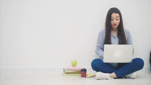 Asiatiska kvinnliga student sitter i lotos position, med bärbar dator, dricka kaffe. Hon har ont i fingertopparna på grund av maskinskrivning. — Stockvideo