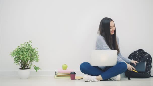 Asiatische Dame sitzt auf dem Boden in lotos Position, fand etwas Interessantes in ihrem Laptop und beschloss, es in ihr Notizbuch zu kopieren. — Stockvideo