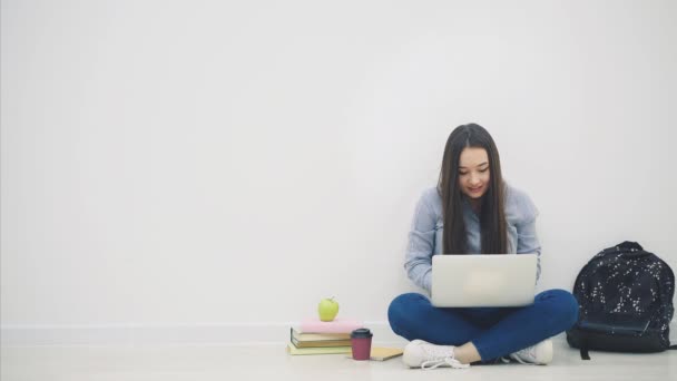 Azjatka siedząca na podłodze w pozycji lotosu, z laptopem, podnosząca ręce, wskazująca na coś bardzo miłego w laptopie, uśmiechnięta szczęśliwie jako zwyciężczyni. — Wideo stockowe