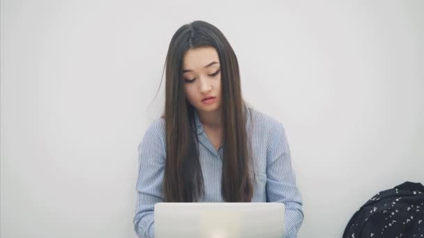 Lovely young asian lady sitting, with laptop, raising a sheet of paper with question mark written on it, nodding her head, understanding nothing. Cheerless face expression. — Stock Video