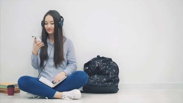 Gadis Asia muda yang terilhami duduk di lantai, melakukan pekerjaan rumah, mendengarkan musik, beralih dari lagu, menari . — Stok Video