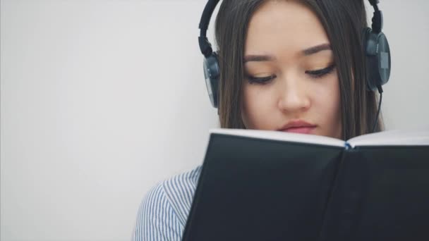 Ihletett fiatal ázsiai lány ül a padlón fülhallgatóban, zenét hallgat, ír, felnéz a kamerára, mosolyog. — Stock videók
