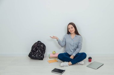 Güzel gülümseyen Asyalı öğrenci loto pozisyonu almış, etrafı öğrenim malzemeleriyle çevrili, elini tutuyor, sanki bir şey sunuyormuş gibi..