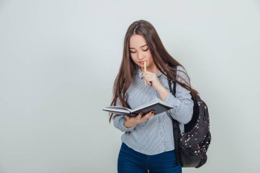 Siyah not defterini açıp ne yazacağını düşünen sevimli Asyalı genç bir kız. Sırt çantası omzuna asılmış..