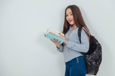 Asyalı güzel bir kız, elinde mavi bir kitapla sayfaları çeviriyor. Sırt çantası omzuna asılmış..