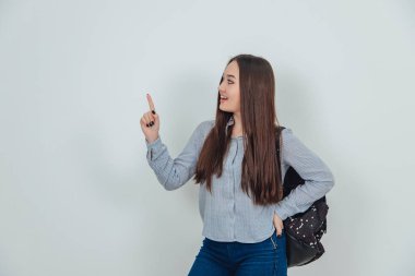 Sırt çantasını omzuna dayayıp parmağını kaldırmış çekici Asyalı genç bir kız..