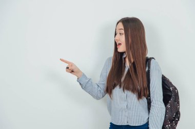 Sırt çantasını omzuna asmış çekici Asyalı genç kız parmağını yan tarafa uzatıp işaret ediyor..