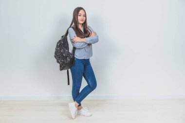 Sırt çantalı, elleri bağlı, bacak bacak üstüne atmış, kendinden emin, havalı Asyalı genç kız..