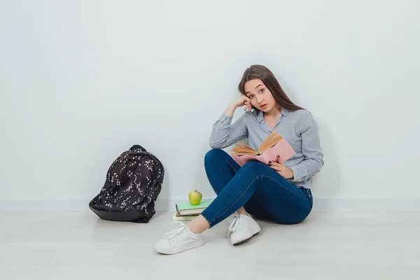 Mladá asijská dívka zapojená do procesu čtení knihy, zatímco sedí na podlaze se zkříženýma nohama. — Stock fotografie