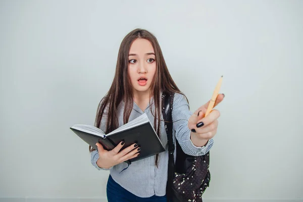 Young journalist. Cute young asian girl standing with notebook, pointing at someone as if giving a right to speak. Backpack slung over her shoulder.