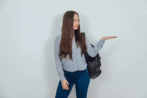 Inspirado joven asiática chica de pie con mochila colgada sobre su hombro, levantando su palma abierta con copyspace para texto o producto . —  Fotos de Stock