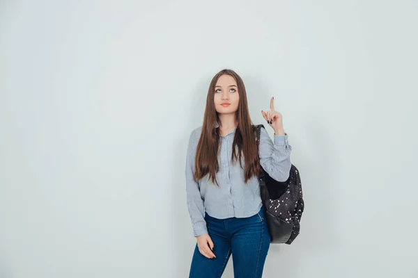 Attractive young asian girl standing with backpack slung over her shoulder, looking and pointing her finger up. — Stock Photo, Image