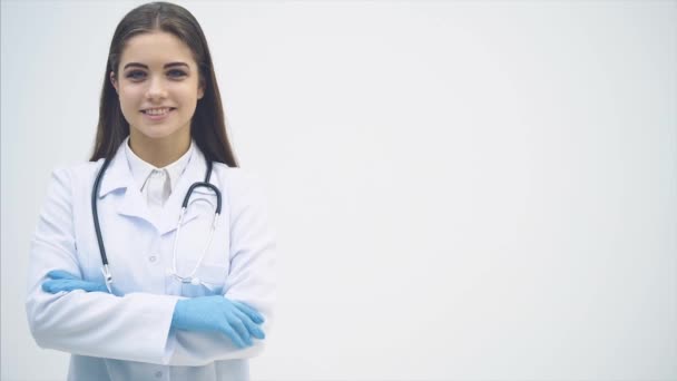 Ung kvinnlig praktikant stående i medicinsk uniform, tittar på kameran, ler, händerna vikta. — Stockvideo