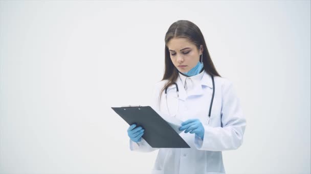 Joven pasante de pie en uniforme médico, sujetando el portapapeles, revisando datos, asintiendo con la cabeza, volteando páginas . — Vídeos de Stock