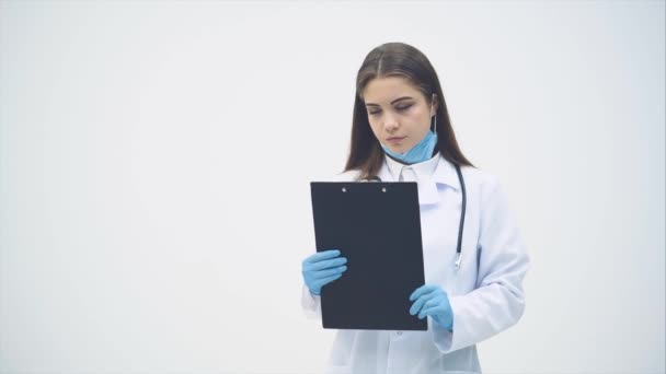 Jonge vrouwelijke stagiaire in medisch uniform, klembord vasthouden, kijken naar de camera met ernstige fsce uitdrukking. — Stockvideo