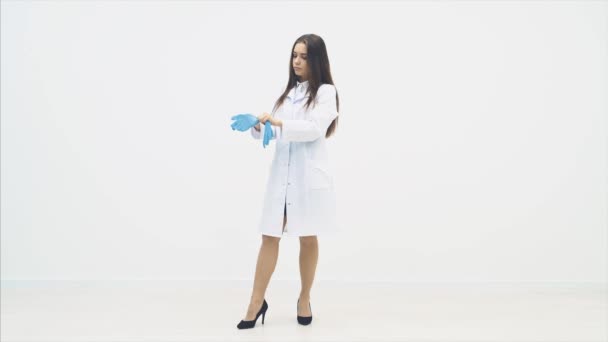 Full-length confident female intern standing, wearing blue medical disposable gloves, approaching the camera, then video becomes bluurred. — ストック動画