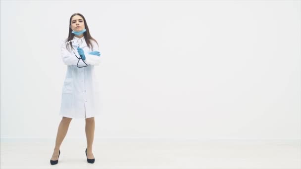 Jeune femme médecin pleine longueur apparaissant sur le fond blanc, tenant stéthoscope, posant, les mains pliées . — Video