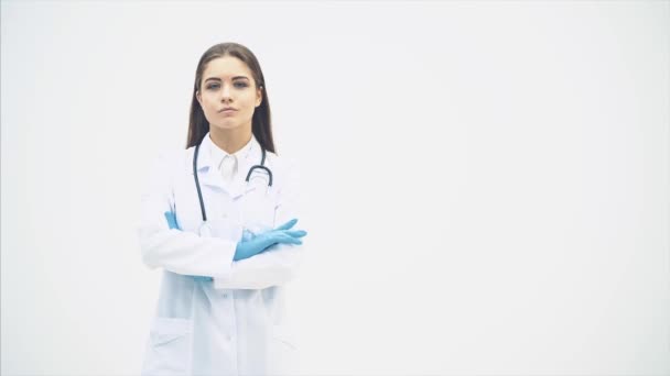 Genç bayan doktor tıp üniforması içinde duruyor, kameraya konsantre yüz ifadesiyle bakıyor, poz veriyor, ellerini katlıyor.. — Stok video