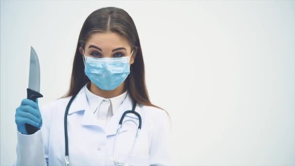 Verdachte jonge vrouwelijke arts met medisch masker met groot scherp mes in haar hand, knikken haar hoofd, onheilspellend kijken. — Stockvideo