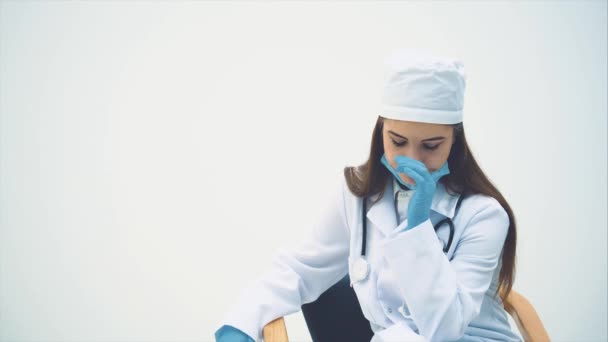 Young female doctor sitting in the chair, taking off the medical mask, massaging her temple, sighing heavily. — Stock Video