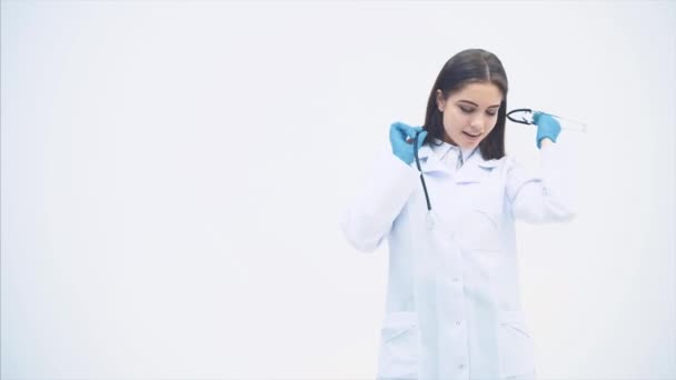 Hermosa doctora poniendo estetoscopio sobre su cuello, levantando cejas, mirando tentadoramente, posando, coqueteando . — Vídeos de Stock