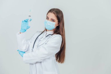 Tıbbi maskeli, elinde şırıngayla gülümseyen kendine güvenen kadın doktor..